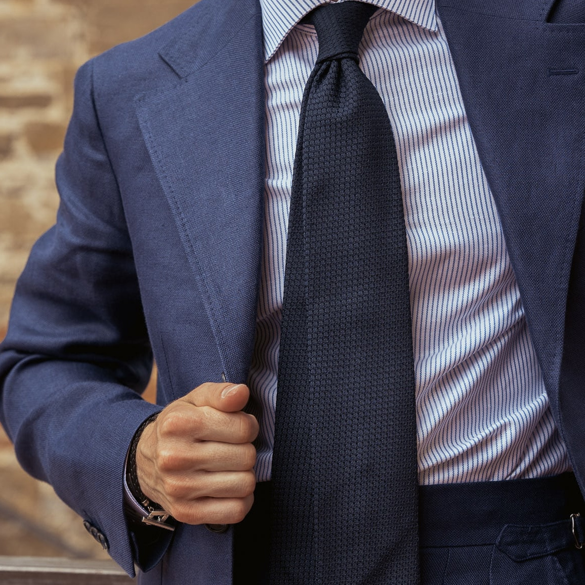 Closeup of a man in a custom navy blue linen suit, striped shirt and textured blue tie