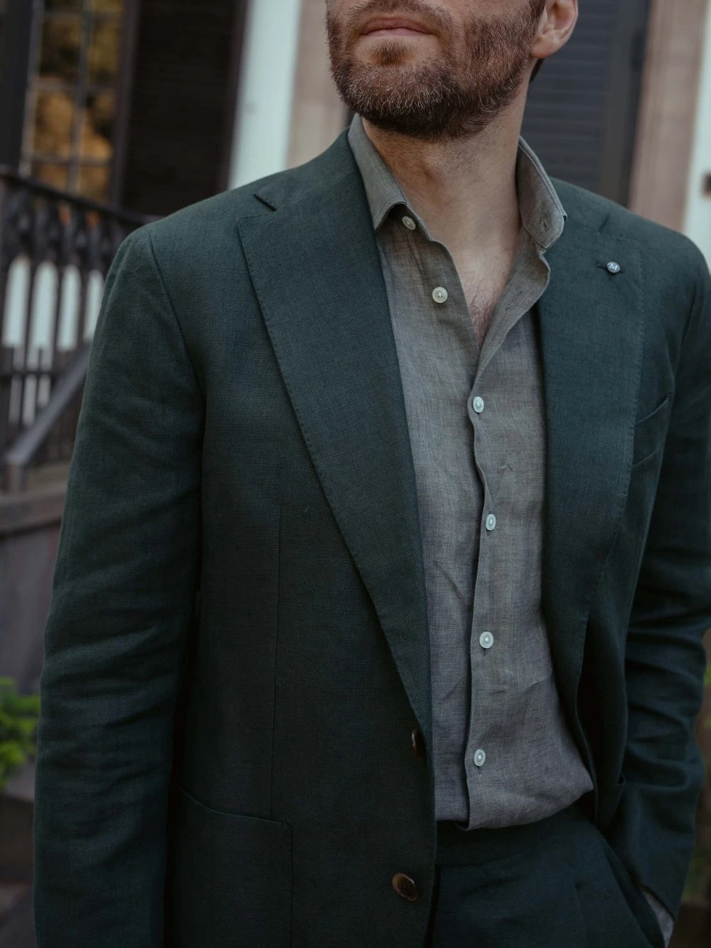 Closeup of man in dark green linen suit and warm-coloured grey linen shirt for a summer wedding