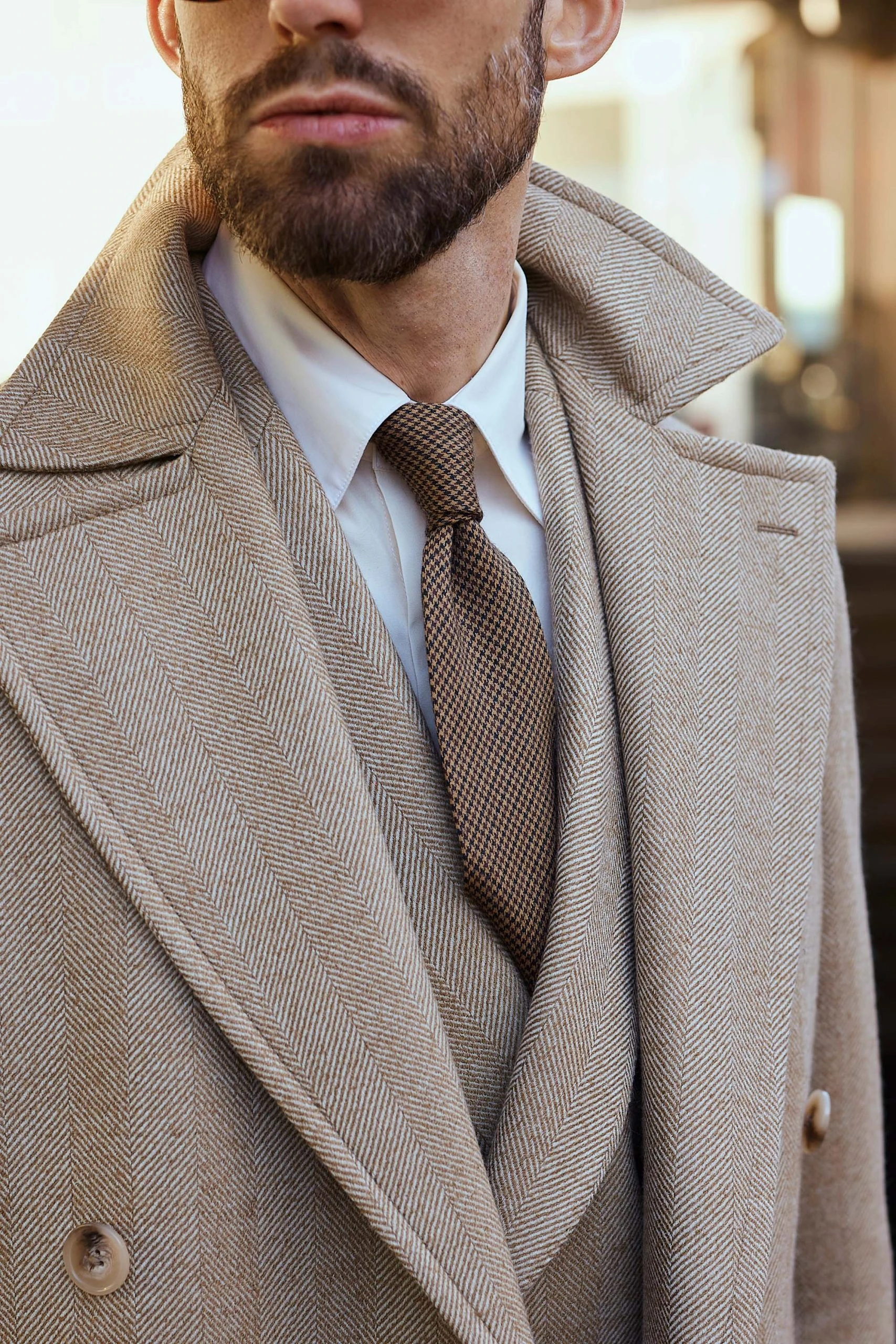 closeup photo of carlos domord at pitti uomo wearing a custom made beige herringbone coat and a matching suit from mond