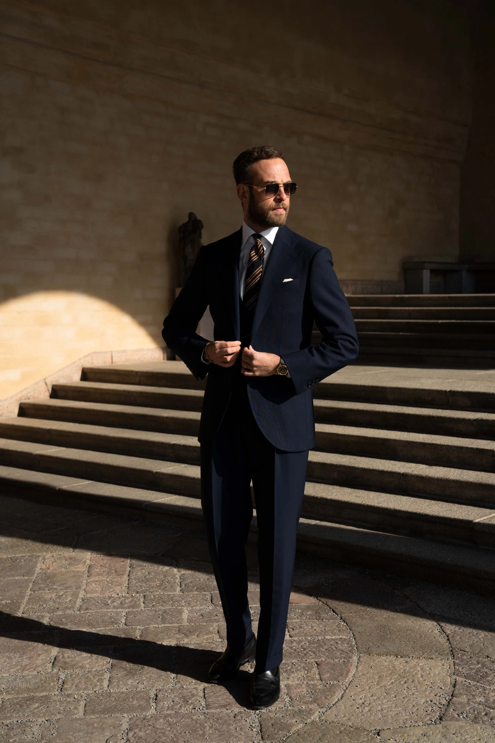 andreas weinas in three piece navy blue suit in twistair, by mond. He is also wearing a striped navy blue and yellow tie, and sunglasses